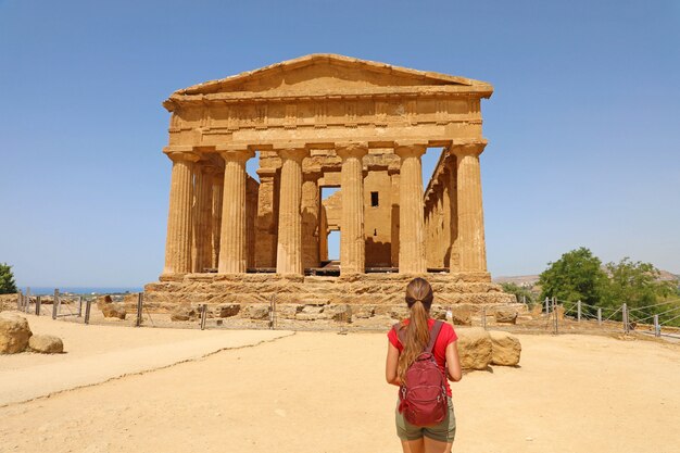 Mulher jovem olha para o Templo da Concórdia no Vale dos Templos de Agrigento, na Sicília. A garota viajante visita templos gregos no sul da Itália.