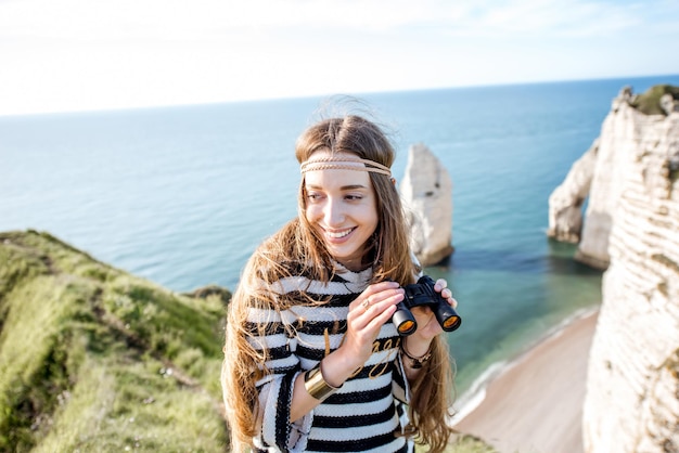Foto mulher jovem olhando com binóculos na famosa costa rochosa perto da cidade de etretat, na frança