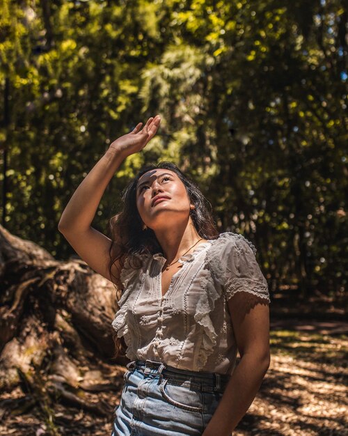Foto mulher jovem olhando para cima enquanto está de pé perto de uma árvore na floresta