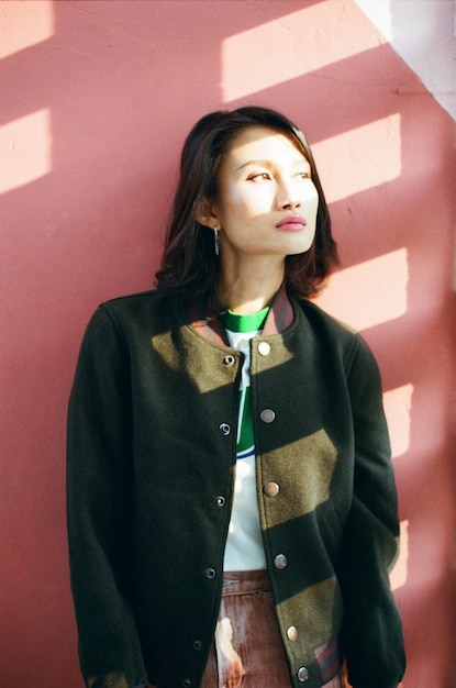 Foto mulher jovem olhando para longe enquanto está de pé contra a parede