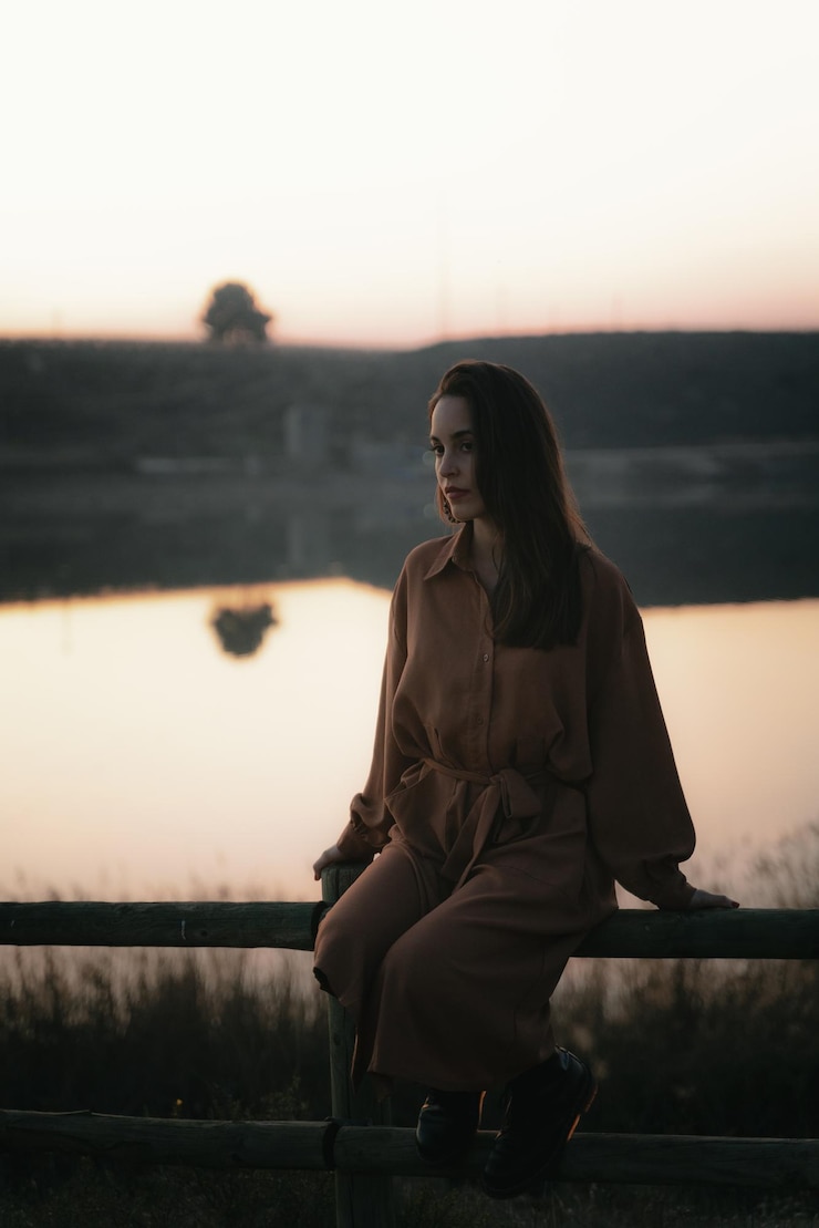 Foto mulher jovem olhando para longe enquanto está sentada em um corrimão contra o céu durante o pôr do sol