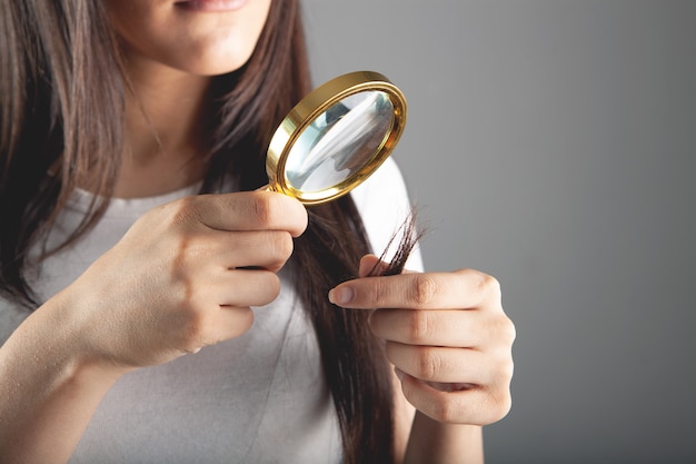 Mulher jovem olhando para o cabelo com uma lupa