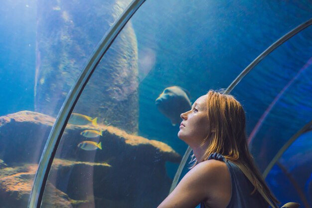 Mulher jovem olhando para peixes em um aquário de túnel.