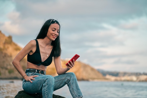 Mulher jovem olhando para um smartphone sentado em uma rocha da praia