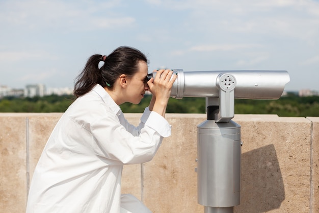 Mulher jovem olhando pelo telescópio binocular de turista