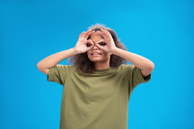 Foto mulher jovem olhando positivamente para a frente usando uma camiseta cor de pêssego mostrando os músculos isolados na parede azul