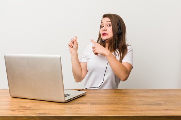 Mulher jovem operador de telemarketing chocado apontando com o dedo indicador para um espaço de cópia.