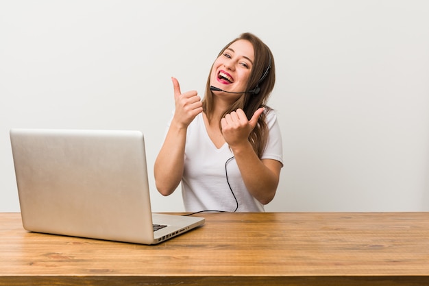 Mulher jovem operador de telemarketing levantando os dois polegares, sorrindo e confiante.