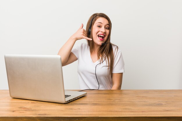 Mulher jovem operador de telemarketing mostrando um gesto de chamada de telefone móvel com os dedos.