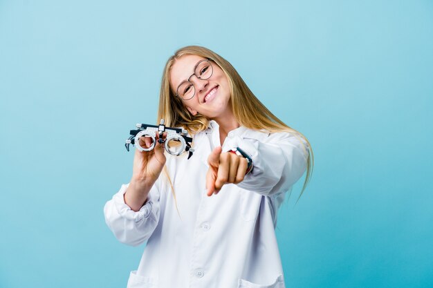 Mulher jovem optometrista russa em sorrisos alegres azuis, apontando para a frente.