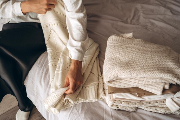Mulher jovem organizando roupas de tricô quentes na cama