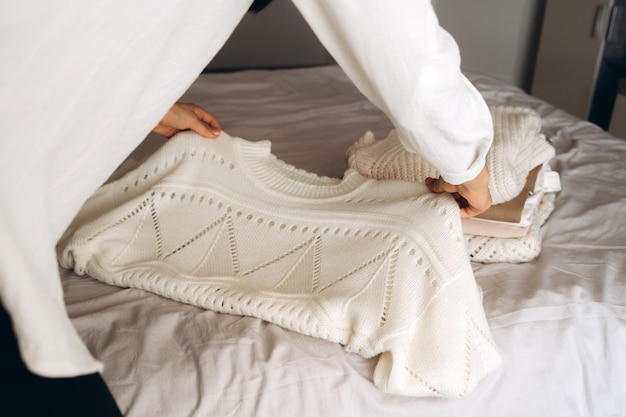 Mulher jovem organizando roupas de tricô quentes na cama