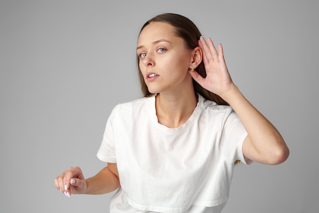 Foto mulher jovem ouvindo com a mão sobre uma orelha em fundo cinzento