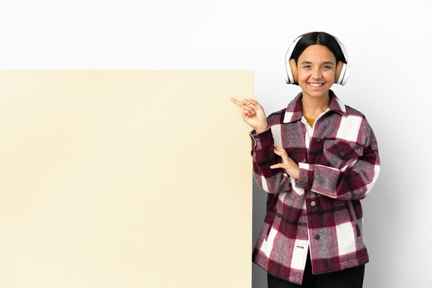 Mulher jovem ouvindo música com um grande fundo de cartaz vazio isolado apontando para o lado para apresentar um produto