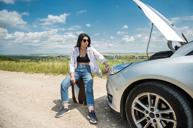 Mulher jovem parece sob o capô do motor como motor de carros quebrados. Quebra de carro na estrada. Férias interrompidas