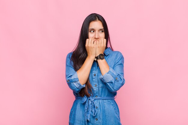 Mulher jovem parecendo preocupada, ansiosa, estressada e com medo, roendo as unhas e olhando para o espaço da cópia lateral