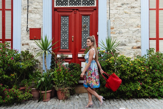 Mulher jovem passeando por uma casa histórica com portas vermelhas e um monte de diferentes plantas e flores em uma aldeia mediterrânea