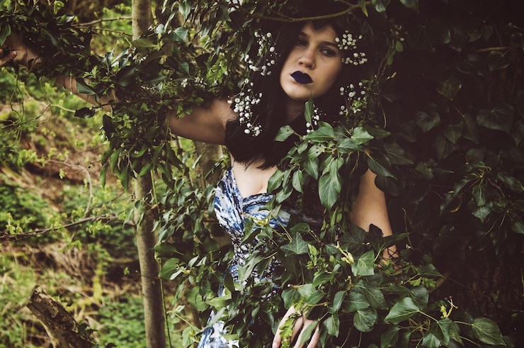 Foto mulher jovem pensativa com maquiagem usando flores em meio a folhas na floresta