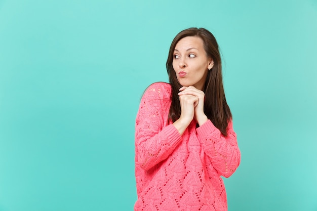 Mulher jovem pensativa no suéter rosa tricotado, olhando de lado, colocou o apoio da mão no queixo isolado no fundo da parede azul, retrato de estúdio. Emoções sinceras de pessoas, conceito de estilo de vida. Simule o espaço da cópia.