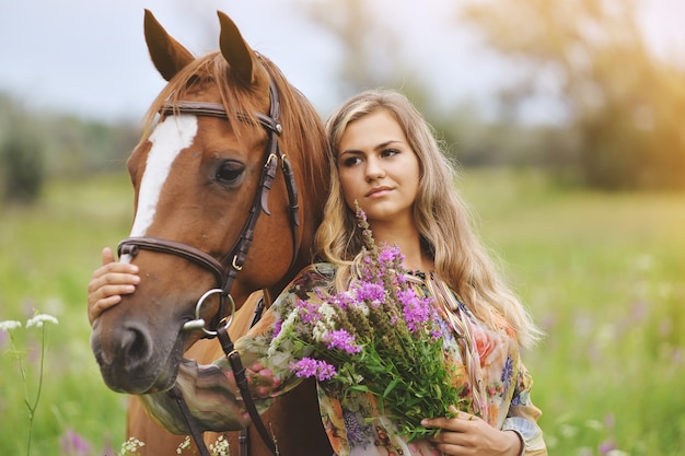 Mulher jovem perto de um cavalo com um vestido de verão em um prado
