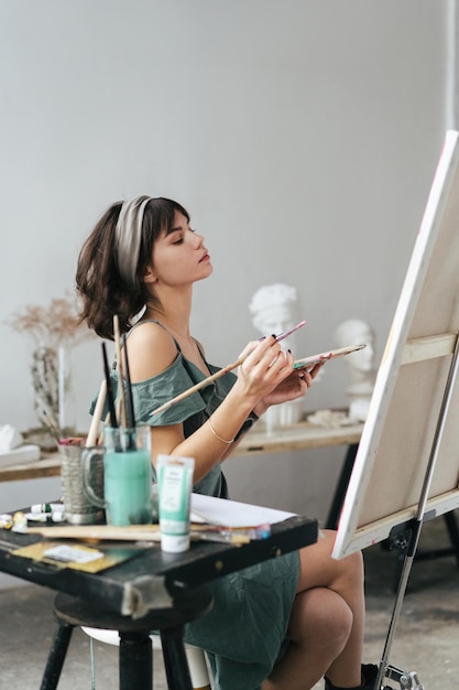 Mulher jovem pintando em tela enquanto está sentada na mesa