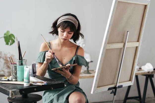 Mulher jovem pintando em tela enquanto está sentada na mesa