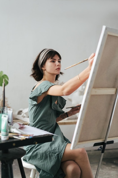 Mulher jovem pintando em tela enquanto está sentada na mesa