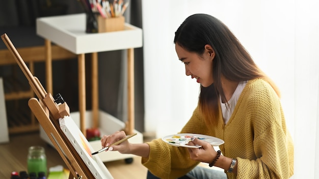 Mulher jovem pintando em uma tela em casa