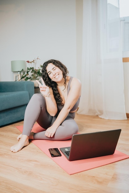 Mulher jovem plus size sentada sobre um tapete de ioga enquanto treina em casa on-line com um conceito de curso on-line para laptop Copiar treino de imagem de espaço em casa para perder peso antes do verão