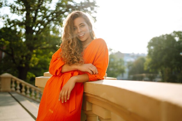 Foto mulher jovem posando contra o pano de fundo da paisagem urbana em vestido laranja brilhante conceito de estilo de vida