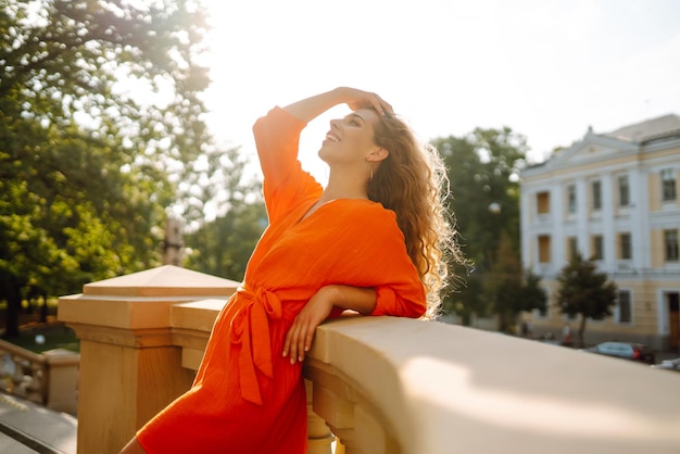 Mulher jovem posando contra o pano de fundo da paisagem urbana em vestido laranja brilhante Conceito de estilo de vida