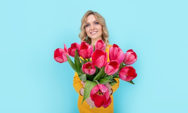Mulher jovem positiva com flores de tulipa de primavera em fundo azul 8 de março
