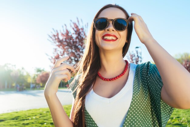 Mulher jovem positiva em óculos de sol, caminhando no parque, rindo. dia ensolarado