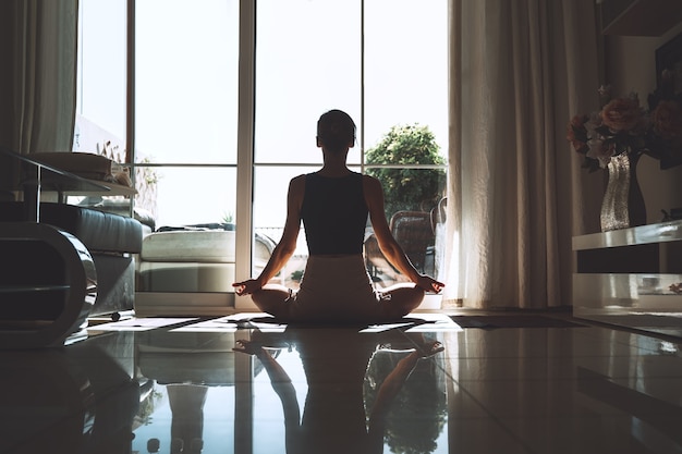 Mulher jovem praticando ioga dentro de casa. Linda garota meditando e fazendo poses de ioga em casa