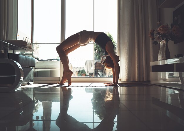 Mulher jovem praticando ioga dentro de casa. Linda garota meditando e fazendo poses de ioga em casa