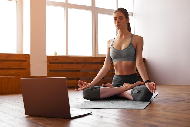 Mulher jovem praticando ioga em casa Treinamento em vídeo on-line Menina fazendo exercícios e meditando Yoga equilíbrio meditação relaxamento estilo de vida saudável autocuidado conceito de aula de treinamento on-line