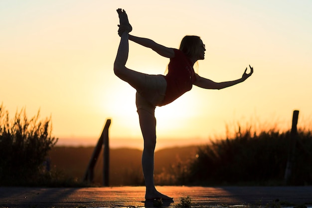 Mulher jovem praticando natarajasana contra o céu claro durante o pôr do sol