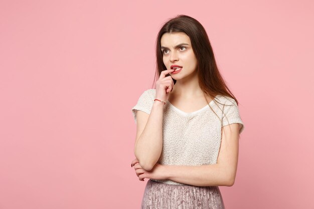 Mulher jovem preocupada em roupas leves casuais posando isolado no retrato de estúdio de fundo de parede rosa pastel. conceito de estilo de vida de emoções sinceras de pessoas. mock up espaço de cópia. olhando para roer unhas.