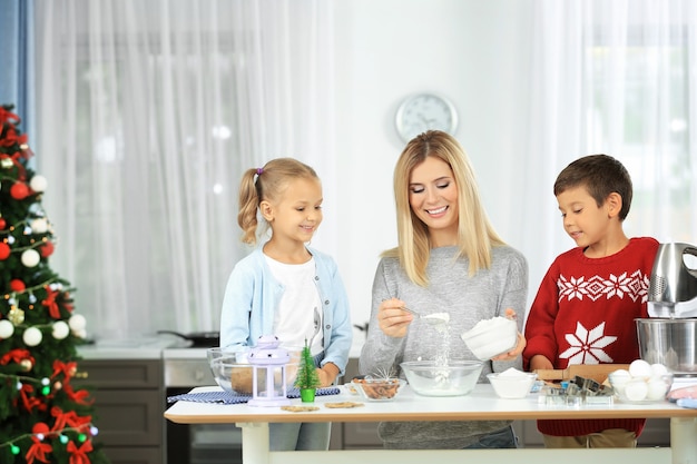 Mulher jovem preparando biscoitos de Natal com crianças pequenas na cozinha