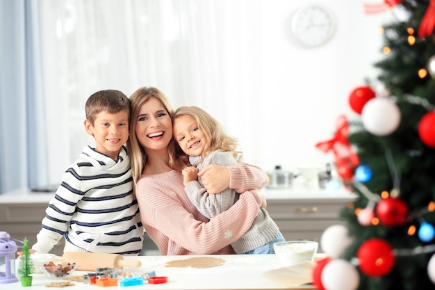 Mulher jovem preparando biscoitos de Natal com crianças pequenas na cozinha