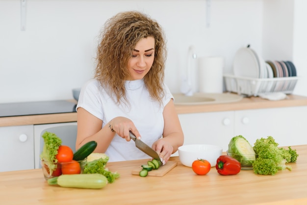 Mulher jovem preparando salada de legumes na cozinha dela.