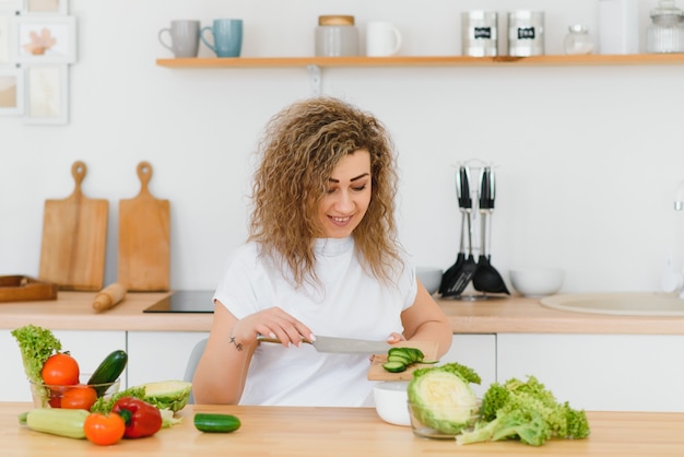 Mulher jovem preparando salada de legumes na cozinha dela.