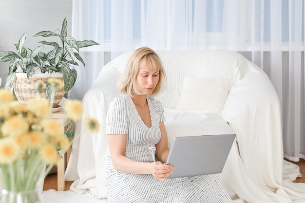 Mulher jovem que trabalha em casa. Freelancer, usando laptop, telefone e Internet.