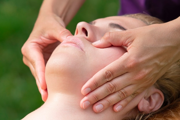 Mulher jovem recebendo massagem facial com mãos de médico ao ar livre em fundo natural desfrutando