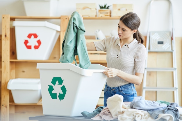 Mulher jovem reciclando seu guarda-roupa ela jogando suas roupas no lixo