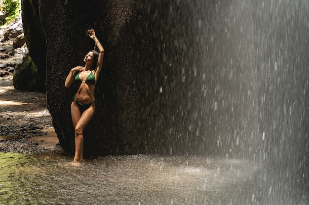 Foto mulher jovem relaxada de olhos fechados enquanto ouve os sons da cachoeira, conceito tropical