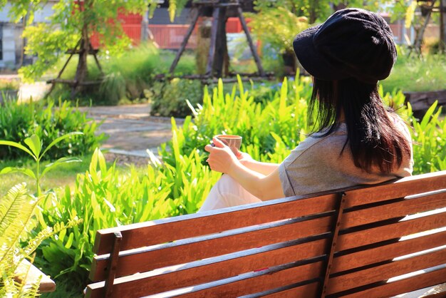 Mulher jovem relaxando em um banco com uma xícara de café no jardim