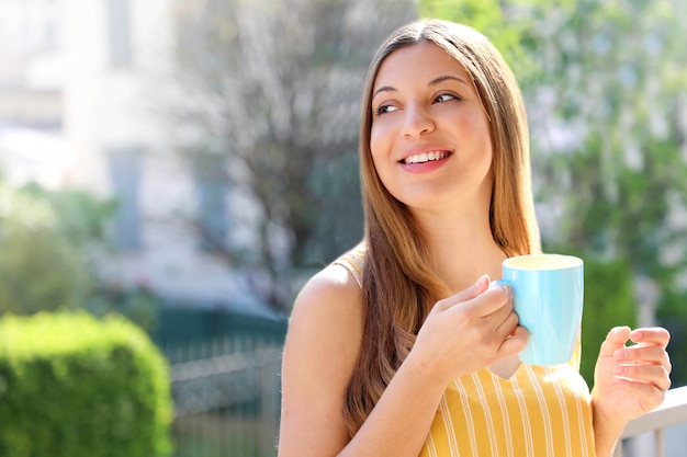 Mulher jovem relaxando na varanda segurando uma caneca de cappuccino ou chá em casa pela manhã