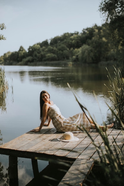 Mulher jovem relaxante em um píer de madeira no lago calmo