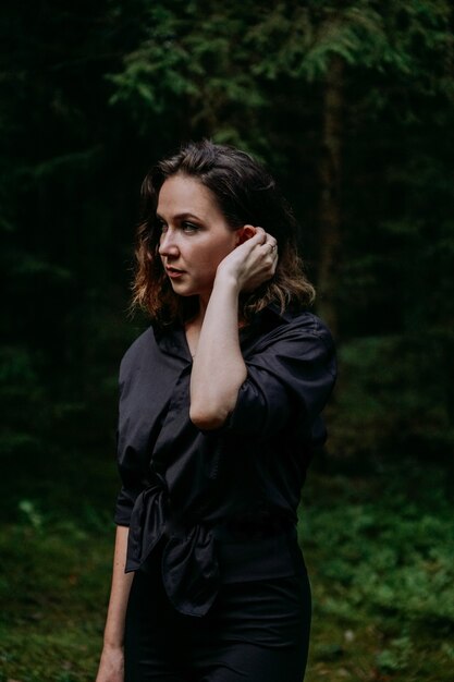 Mulher jovem - retrato próximo em uma floresta de pinheiros escuros. Mulher de camisa preta